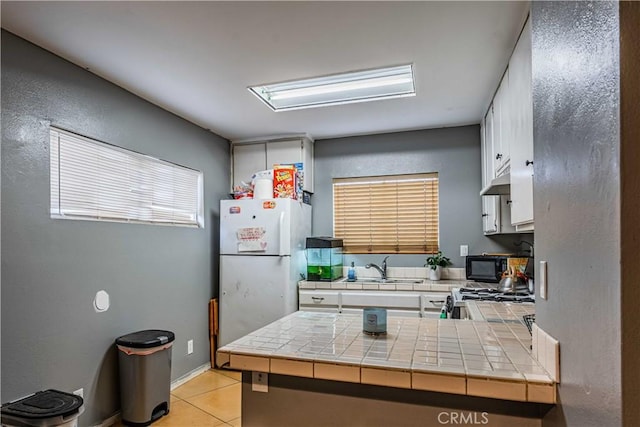 kitchen with light tile patterned flooring, sink, white cabinets, white refrigerator, and tile counters