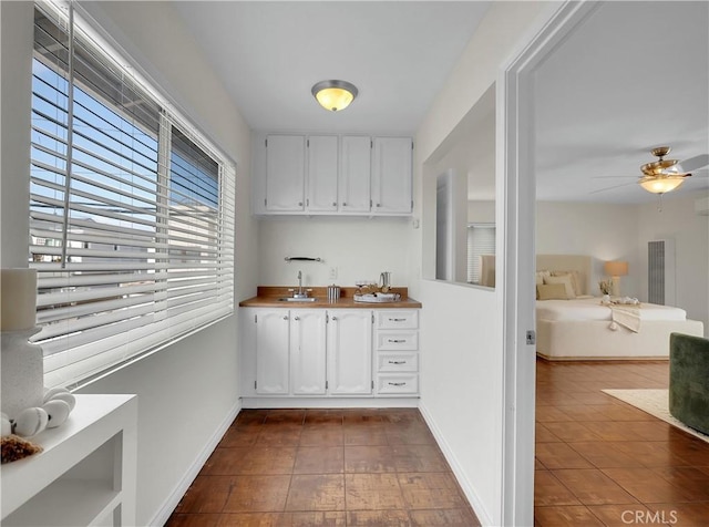 interior space with indoor wet bar, a ceiling fan, a sink, dark tile patterned floors, and baseboards