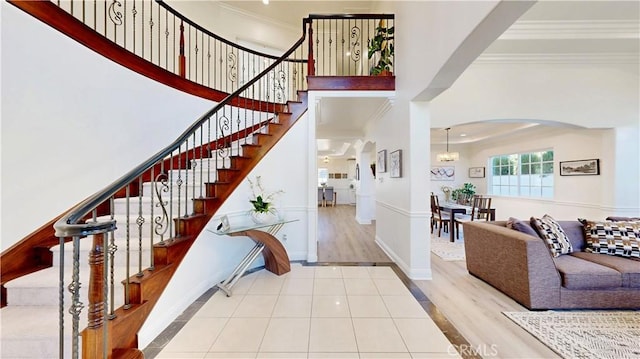 tiled foyer entrance with stairs, baseboards, a high ceiling, and crown molding