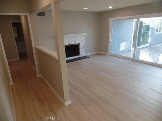 unfurnished living room with a stone fireplace and light hardwood / wood-style floors