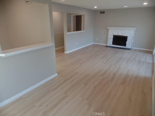 unfurnished living room featuring a stone fireplace and light hardwood / wood-style floors