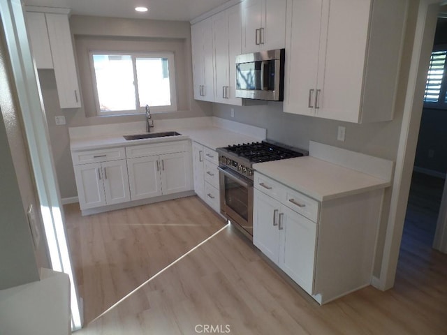 kitchen with sink, light wood-type flooring, white cabinets, and appliances with stainless steel finishes