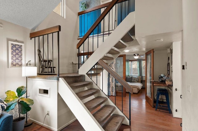 stairway featuring high vaulted ceiling, hardwood / wood-style floors, and a textured ceiling