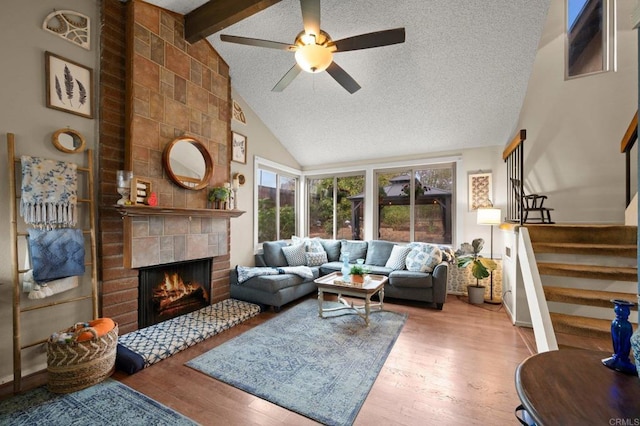 living room featuring a tiled fireplace, wood-type flooring, a textured ceiling, and beam ceiling