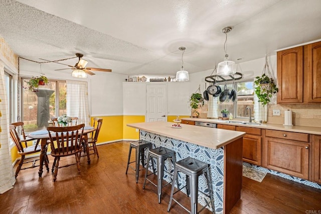 kitchen with dark wood-type flooring, a kitchen bar, sink, hanging light fixtures, and a kitchen island