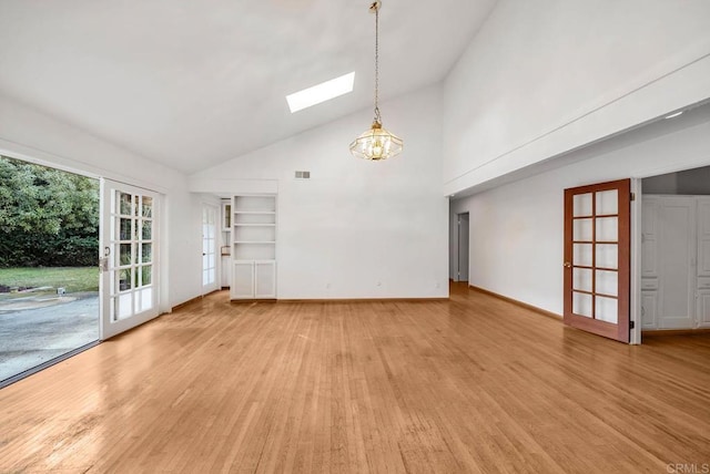 unfurnished living room featuring a skylight, french doors, baseboards, and light wood finished floors