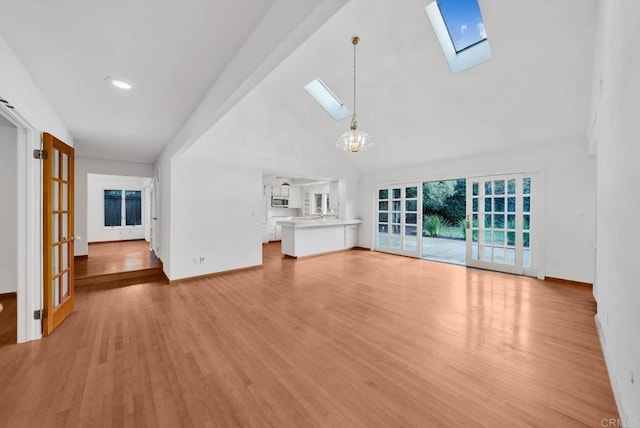 unfurnished living room with high vaulted ceiling, a notable chandelier, a skylight, baseboards, and light wood finished floors