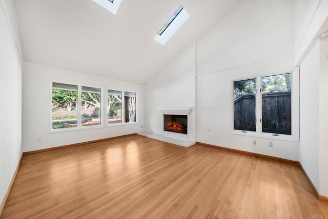 unfurnished living room with high vaulted ceiling, light wood-type flooring, a fireplace, and a skylight