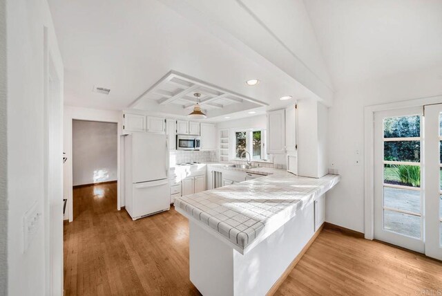 kitchen featuring tile countertops, stainless steel microwave, freestanding refrigerator, white cabinets, and a peninsula