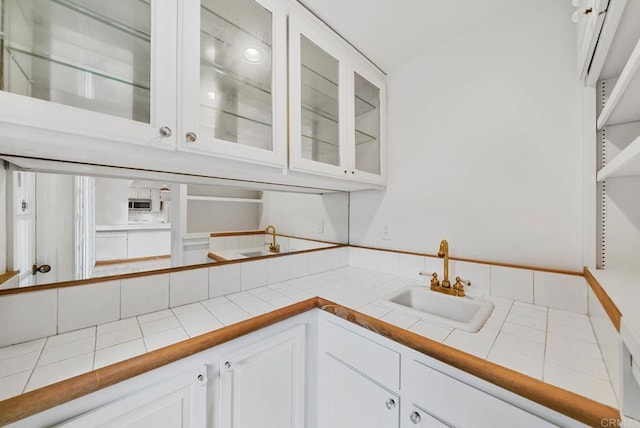 kitchen featuring glass insert cabinets, tile counters, white cabinetry, and a sink