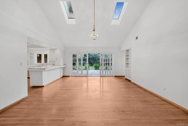 unfurnished living room with a chandelier, light wood finished floors, baseboards, and built in features