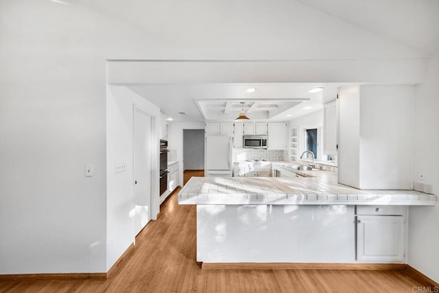 kitchen featuring a peninsula, a sink, white cabinets, stainless steel microwave, and white built in refrigerator