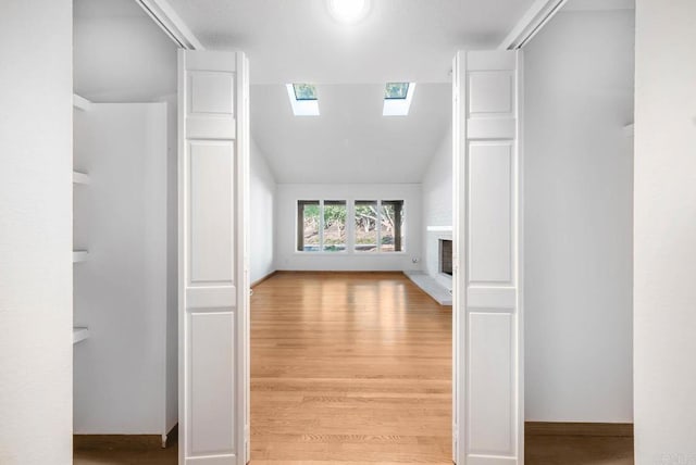 bonus room with a fireplace with raised hearth, light wood finished floors, a skylight, and baseboards