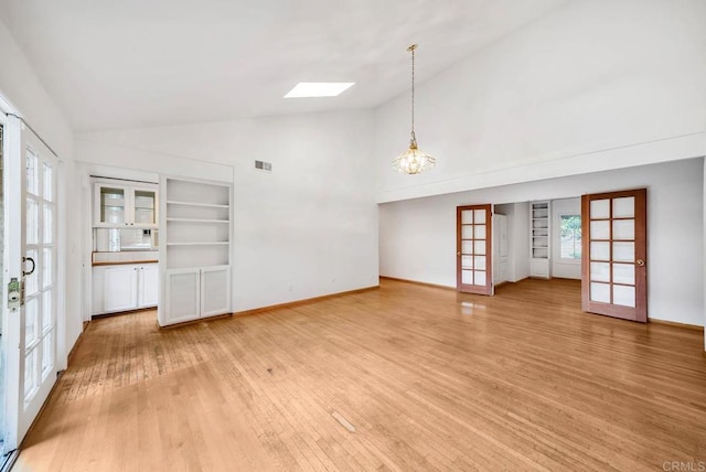 unfurnished living room featuring a skylight, visible vents, an inviting chandelier, french doors, and light wood-type flooring