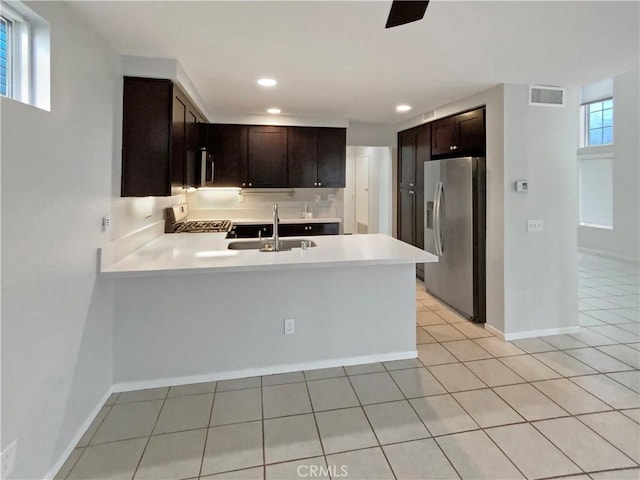 kitchen featuring kitchen peninsula, range, dark brown cabinetry, stainless steel fridge, and sink