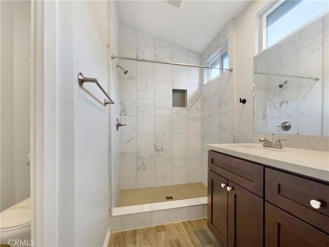 bathroom featuring hardwood / wood-style flooring, toilet, vaulted ceiling, vanity, and tiled shower