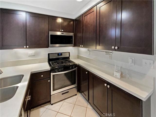 kitchen with light tile patterned flooring, dark brown cabinetry, stainless steel appliances, and sink