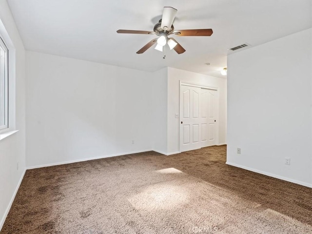 spare room featuring dark colored carpet, a ceiling fan, visible vents, and baseboards