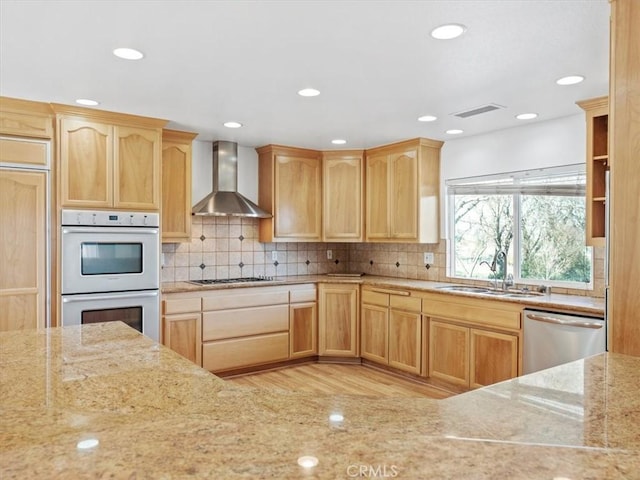 kitchen featuring appliances with stainless steel finishes, a sink, wall chimney range hood, and tasteful backsplash