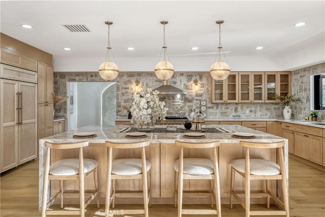 kitchen with paneled built in fridge, light wood finished floors, backsplash, and glass insert cabinets