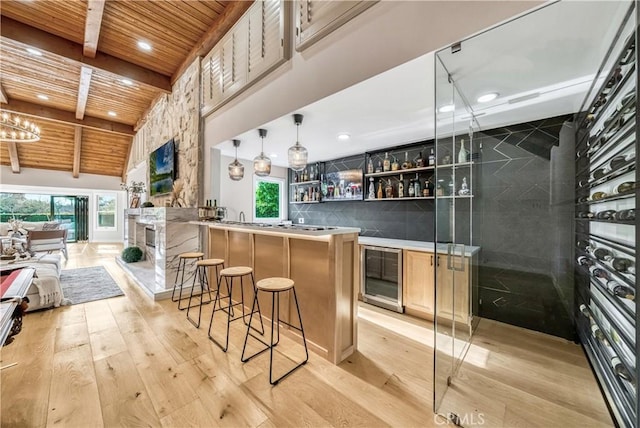 bar with wine cooler, light wood-style flooring, bar area, wooden ceiling, and beam ceiling