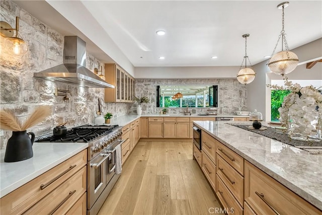 kitchen with light wood finished floors, wall chimney exhaust hood, range with two ovens, light brown cabinets, and tasteful backsplash