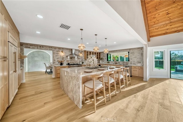 kitchen featuring a large island, wall chimney range hood, light wood-style floors, and visible vents
