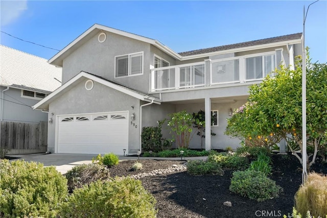 traditional home with a balcony, fence, stucco siding, concrete driveway, and a garage