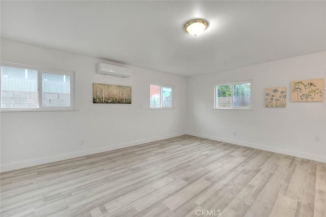 empty room with a wall unit AC, light wood-style floors, and baseboards