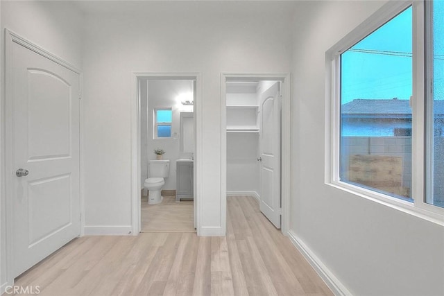 unfurnished bedroom featuring light wood-type flooring, a spacious closet, and multiple windows