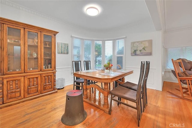 dining space featuring ornamental molding, wainscoting, a decorative wall, and light wood-style flooring