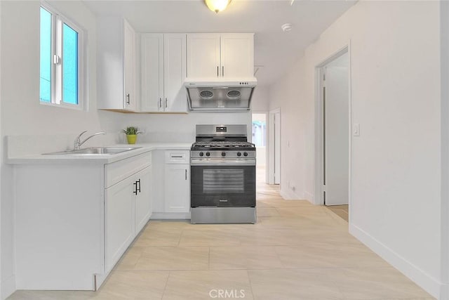 kitchen with stainless steel range with gas stovetop, range hood, light countertops, white cabinetry, and a sink