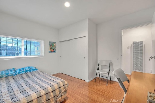 bedroom featuring light wood-style floors, a closet, a heating unit, and baseboards