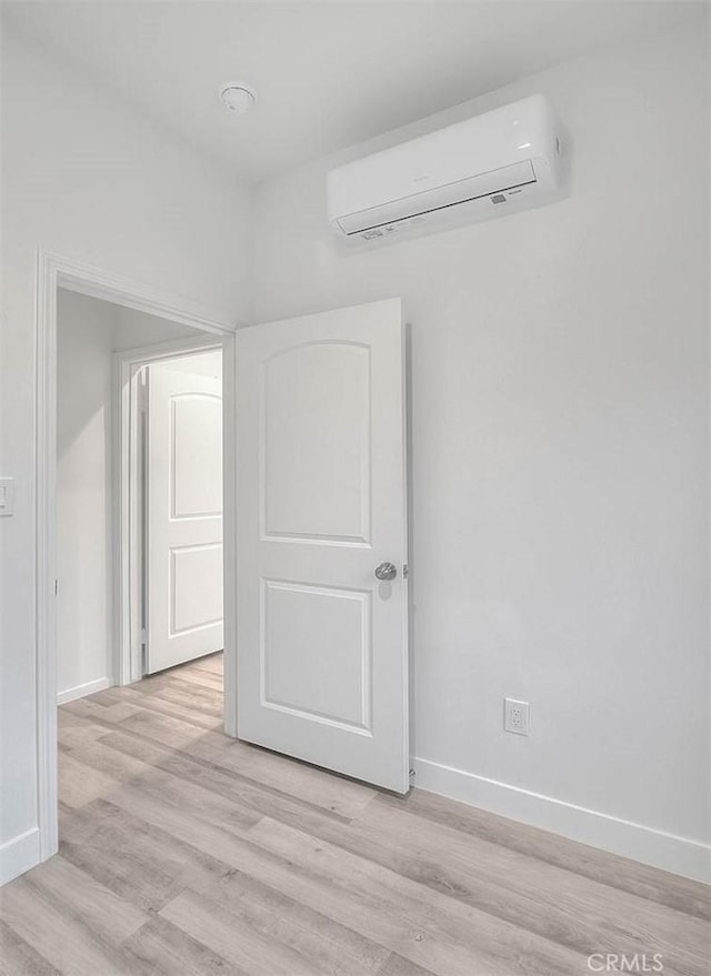 spare room with light wood-style floors, a wall mounted air conditioner, and baseboards