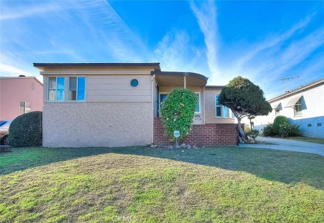 view of side of home featuring stucco siding, brick siding, and a yard