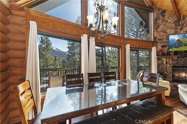 dining room with a stone fireplace, hardwood / wood-style floors, log walls, a chandelier, and a mountain view