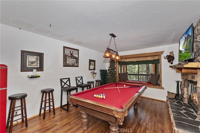 playroom featuring a stone fireplace, dark wood-type flooring, pool table, and a textured ceiling