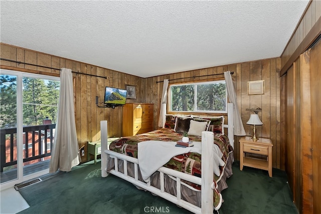 carpeted bedroom with access to outside, a textured ceiling, and wood walls