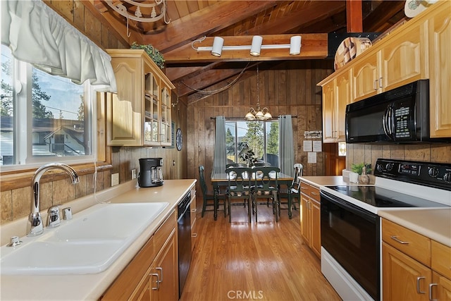 kitchen with wood walls, sink, hanging light fixtures, black appliances, and light hardwood / wood-style flooring