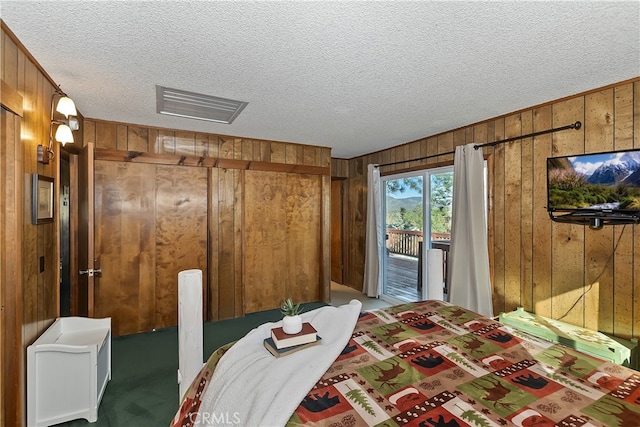 carpeted bedroom featuring access to outside, a textured ceiling, and wood walls