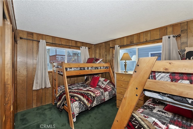 bedroom featuring wooden walls, a textured ceiling, and dark colored carpet