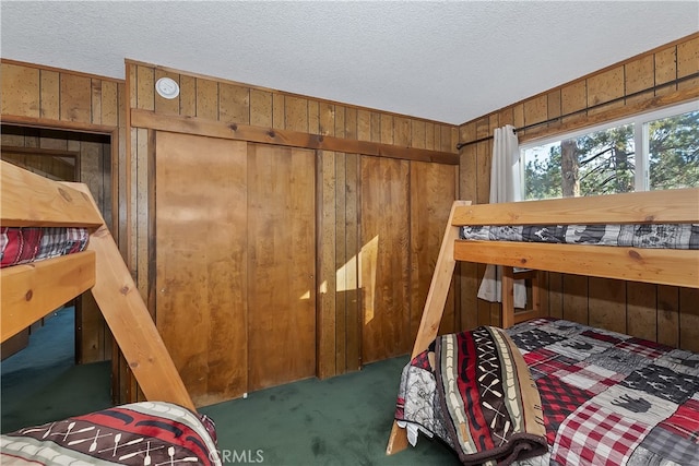 bedroom featuring a textured ceiling, dark carpet, and wood walls