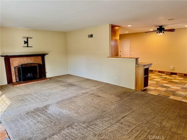 unfurnished living room with carpet, recessed lighting, visible vents, a fireplace with raised hearth, and ceiling fan