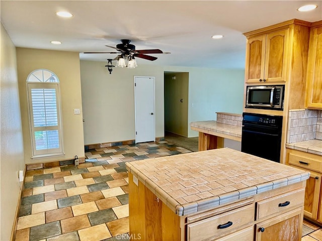 kitchen featuring tile countertops, black oven, stainless steel microwave, and ceiling fan