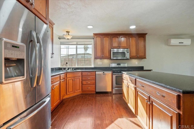 kitchen featuring a wall mounted air conditioner, dark wood-type flooring, a sink, appliances with stainless steel finishes, and dark countertops