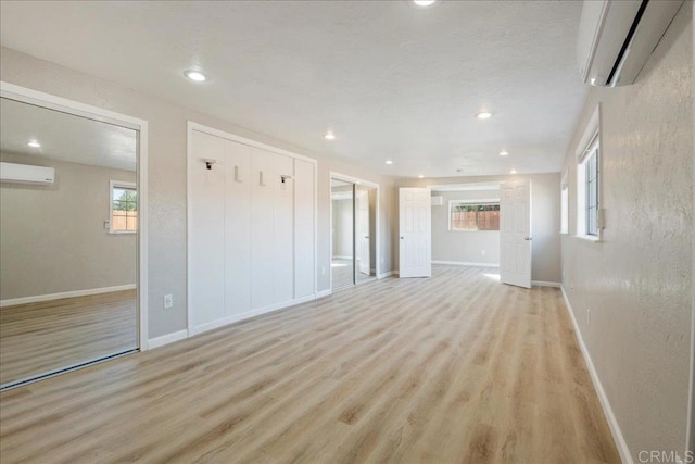 unfurnished living room featuring light wood finished floors, baseboards, and a wall mounted air conditioner