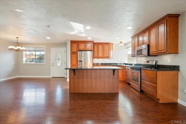 kitchen with brown cabinets, dark countertops, appliances with stainless steel finishes, a breakfast bar area, and dark wood-style flooring