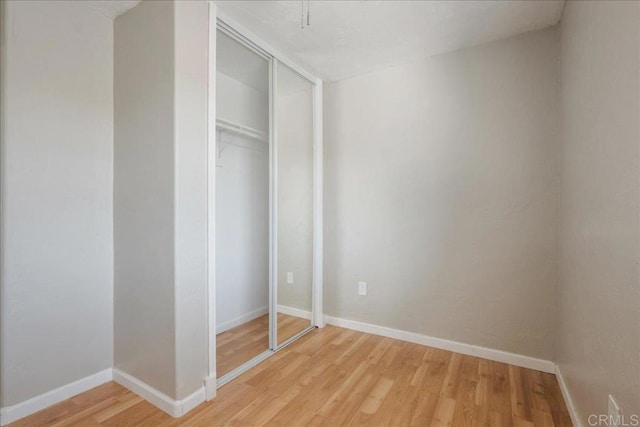 unfurnished bedroom featuring light wood-type flooring, baseboards, and a closet