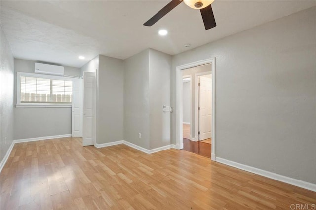 unfurnished room with baseboards, light wood-style floors, and a wall unit AC