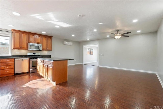 kitchen featuring dark countertops, open floor plan, brown cabinets, appliances with stainless steel finishes, and dark wood-style flooring